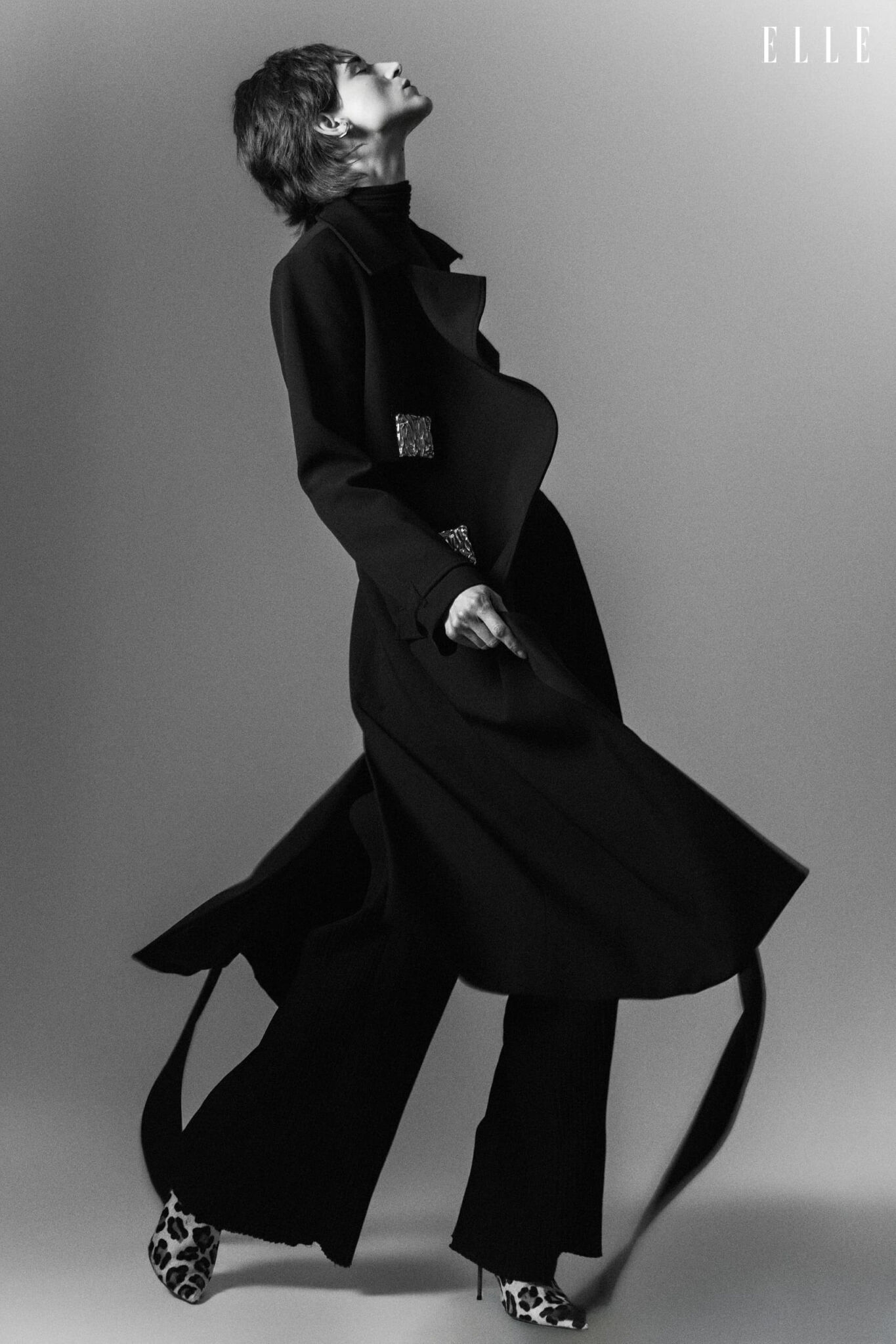 Daiane Conterato in motion in a dark coat, trousers and patterned shoes.