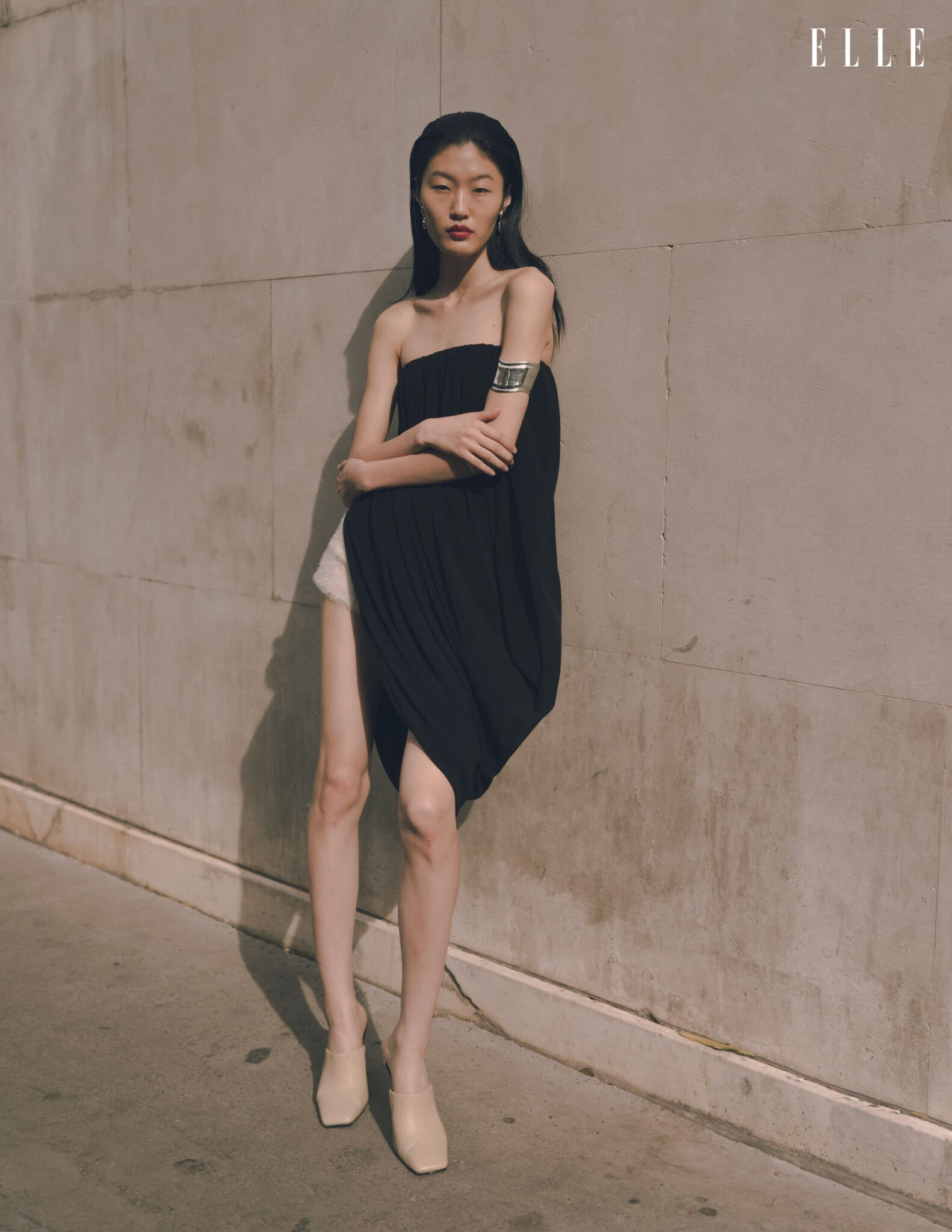 Qian Wen Wu in a sculptural black look against a stone wall