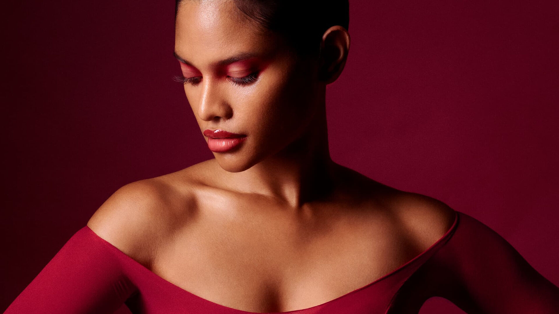 Portrait in a burgundy top against a red backdrop. Photography by Vivi Suthathip.