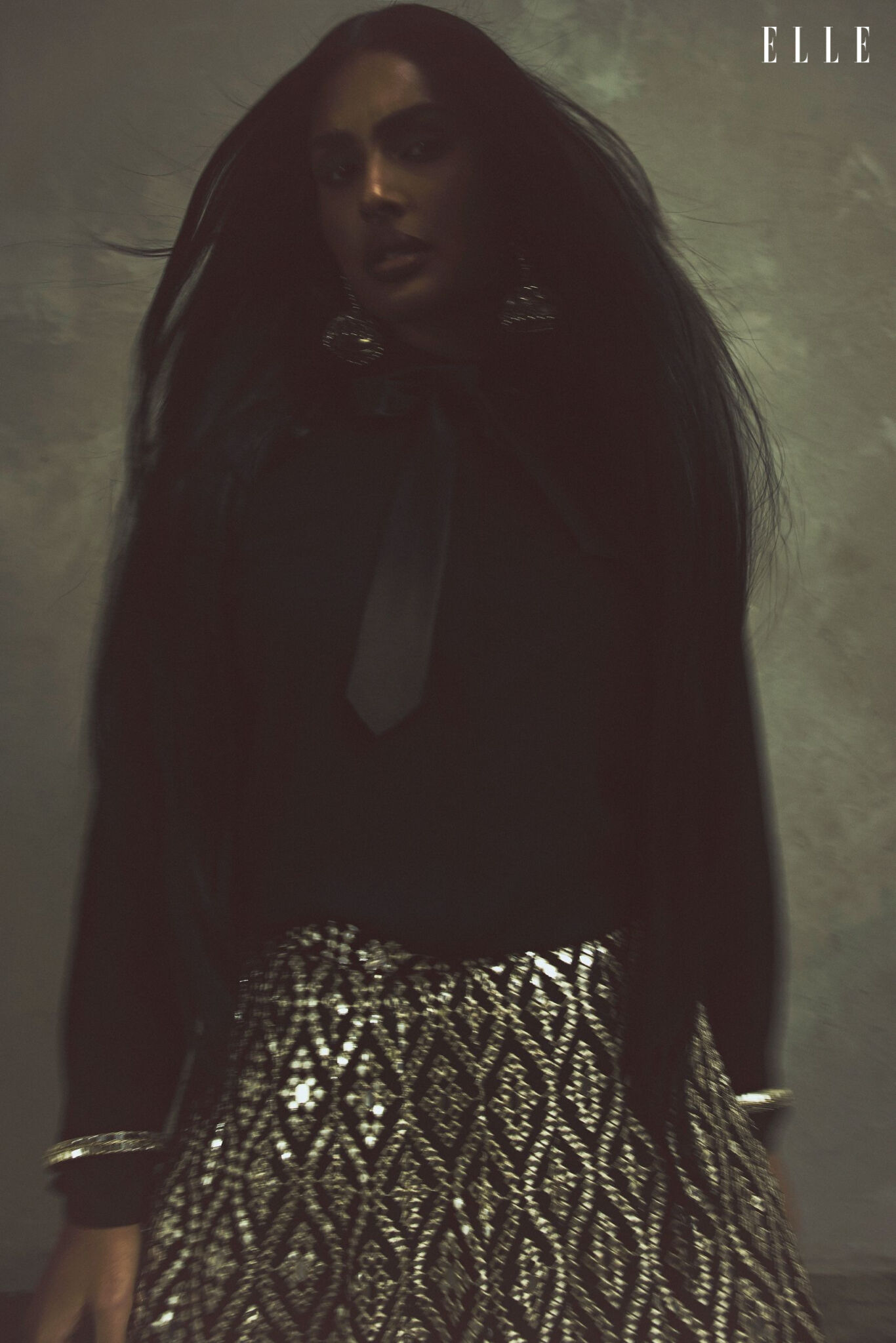 Shanaya Peters in a dark shirt and tie with a patterned Gopi Vaid skirt, photographed in motion.