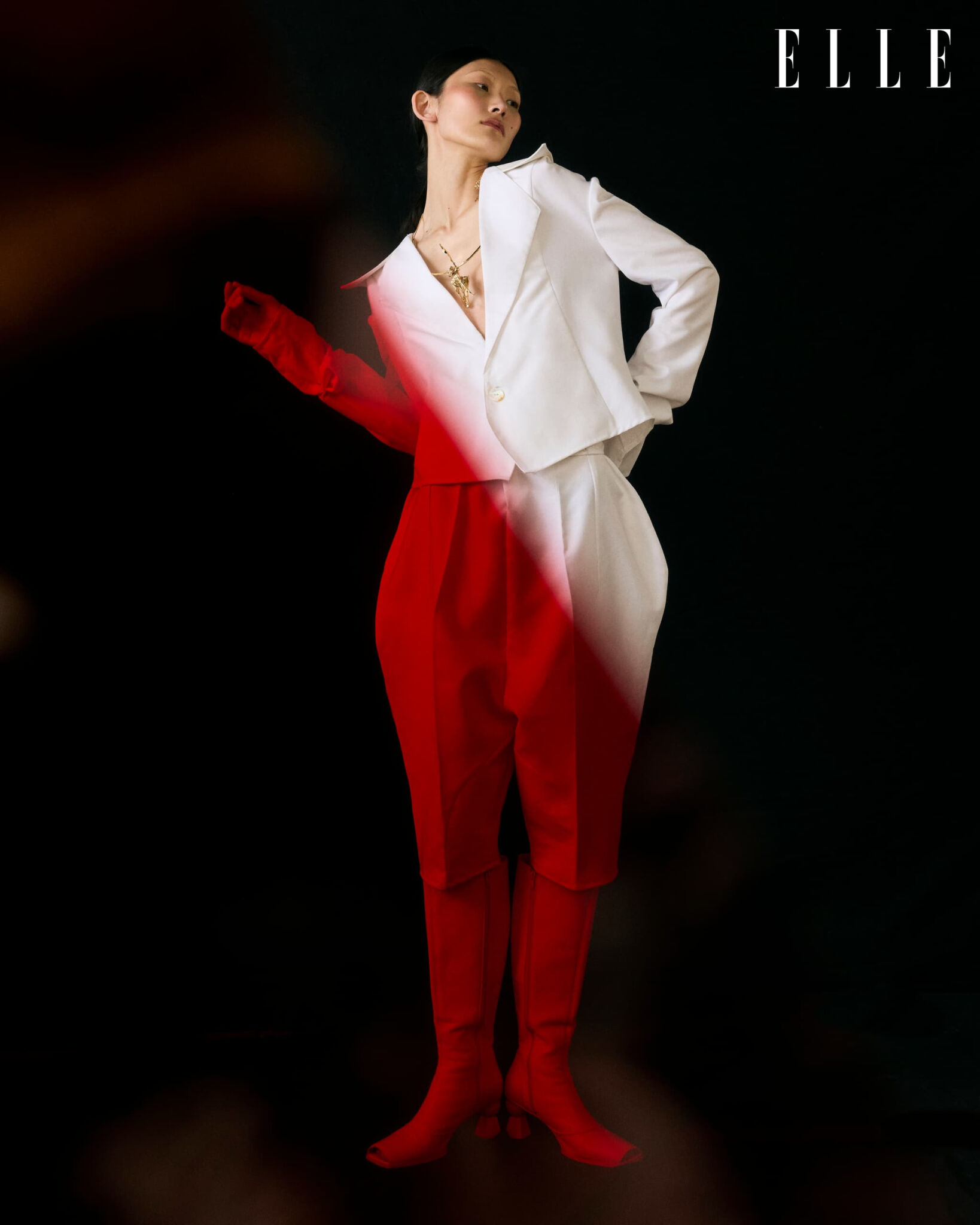 Cheng Peng in a white Atede outfit and Jacquemus boots, lit by a red light effect.