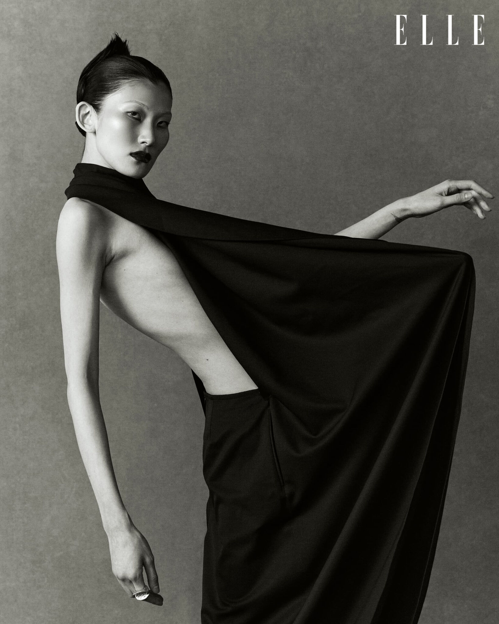 Cheng Peng holding out a black Alaïa jumpsuit in a black-and-white photograph.
